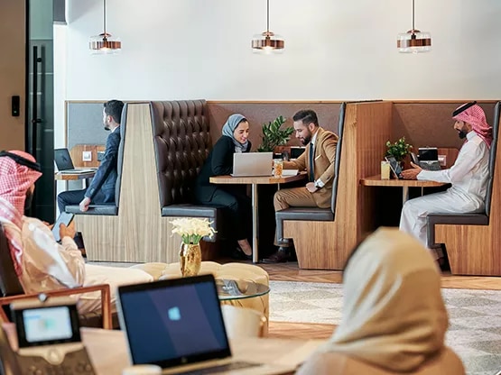 Clients at Servcorp Abu Ouf Plaza in Madinah engage in discussions and focused work within a refined coworking space, featuring private booths and a collaborative atmosphere.